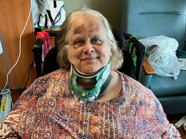Beverly DeMars wearing a printed shirt while wearing a neck brace and smiling.