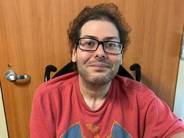 Cody Wallace smiling while seated, wearing a red t-shirt.