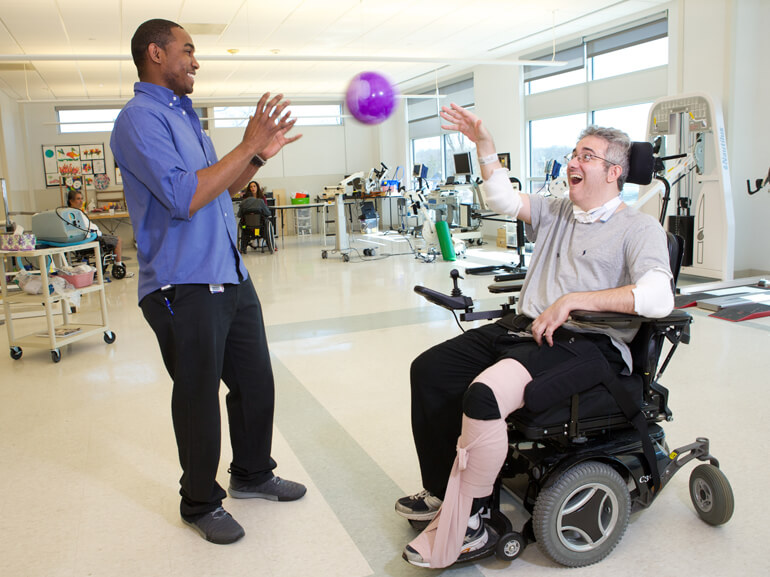physical therapist passing a ball with a patient in a wheelchair