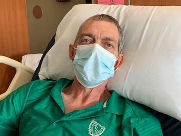 Patient Michael Brown, lying in a hospital bed, wearing a mask