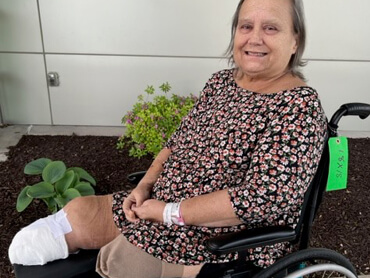 Karen Milburn wearing a floral print shirt seated outdoors in a wheelchair. 