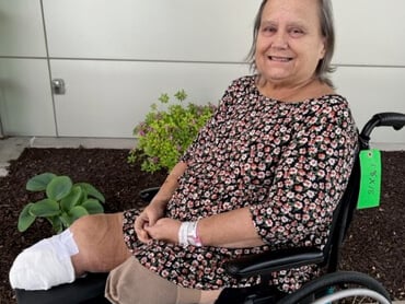 Karen Milburn wearing a floral print shirt seated outdoors in a wheelchair.