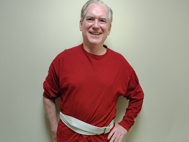 Nick Damato smiling in a red shirt wearing a gait belt. 