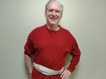 Nick Damato smiling in a red shirt wearing a gait belt.