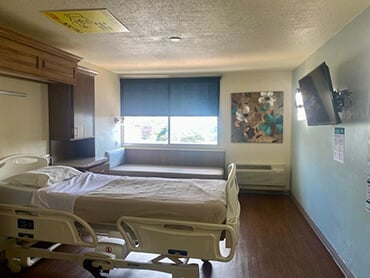 A patient room with a hospital bed, window and TV.