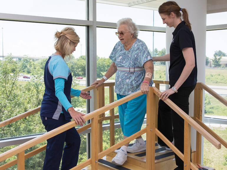 two therapists working with an elderly woman on the training stairs