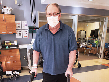 Robert Bretherick, an amputee, is walking with the assistance of a physical therapy walker.