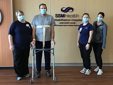 Chad Davis using a walker to help him stand next to three therapists.