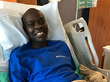 COVID-19 patient Gerald Adory laying in a hospital bed, smiling.