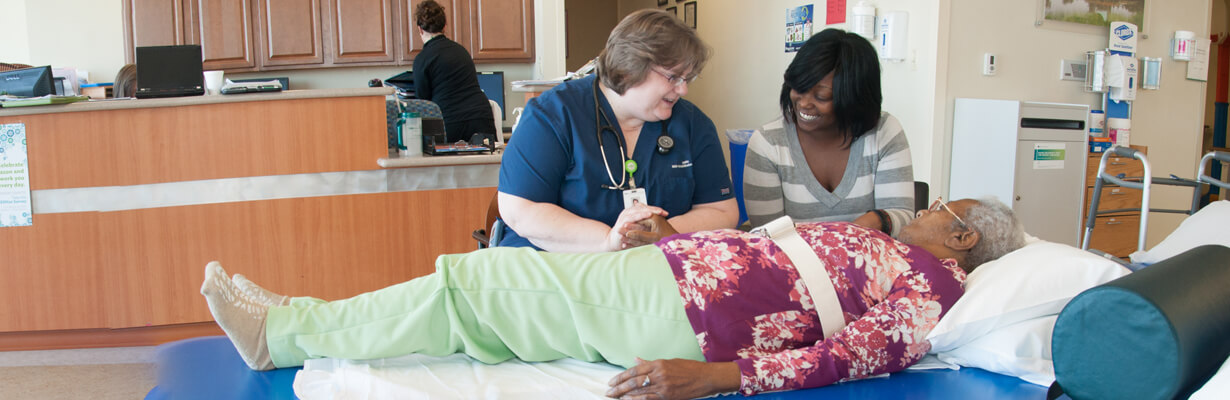 Therapist assisting a patient who is lying on a bed.